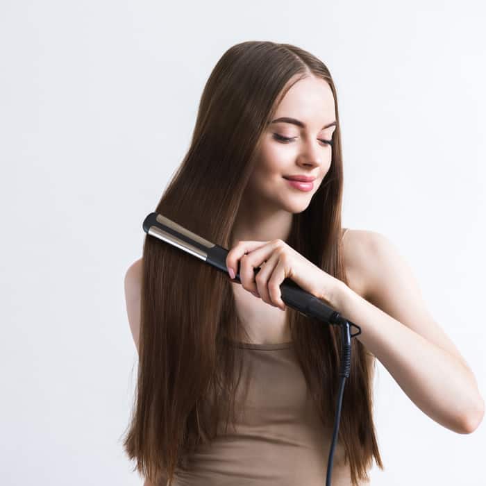  woman using flat iron for long beauty hair